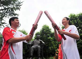 Torchbearer Chen Jing (R) lights the torch for the next torchbearer Li Liangguo in front of the bronze statue of China's late leader Deng Xiaoping during the Beijing 2008 Olympic Games torch relay in Guang'an City, southwest China's Sichuan Province, August 3, 2008. [Xinhua]