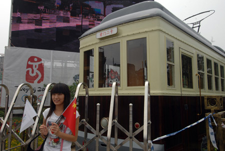 A girl poses for a photo in front of a trail tram, whose service is on suspension to give way to the marathon and other events, on the newly-renovated Qianmen Street in central Beijing, China, Aug. 7, 2008.[Jin Liangkuai/Xinhua]