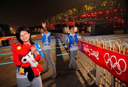 Hu Mengyue (L) and other volunteers have photos taken near the National Stadium, namely the Bird&apos;s Nest, in Beijing, China, at 02:41 on Aug. 8, 2008. The opening ceremony of the Beijing 2008 Olympic Games will be held in the National Stadium at 8 p.m. on Aug. 8.[Xinhua]