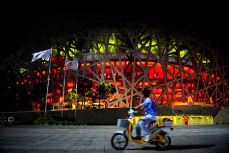 A volunteer rides past the National Stadium, namely the Bird&apos;s Nest, in Beijing, China, at 02:30 on Aug. 8, 2008. The opening ceremony of the Beijing 2008 Olympic Games will be held in the National Stadium at 8 p.m. on Aug. 8. [Xinhua]