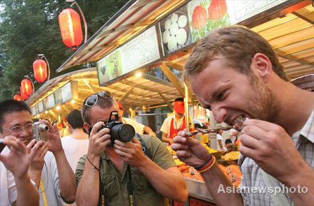People take photos as a foreign tourist eats a snack at the Donghuamen food street in downtown Beijing, August 13, 2008. Centipedes, sharks, scorpions, crickets are all served as delicious food at the night fair on Donghuamen food street. Food stalls thronged with tourists is the common feature on this stretch adjacent to Wangfujing pedestrian street in Beijing. [asianewsphoto]