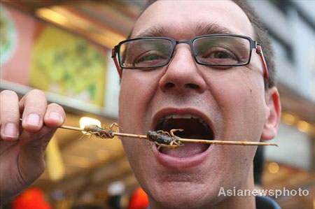 A foreign tourist eats fried scorpions at the Donghuamen food street in Beijing, August 13, 2008. [Asianewsphoto]