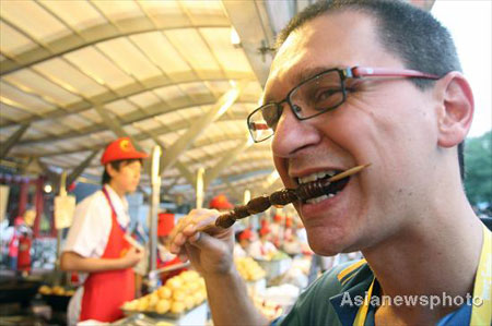 A foreign tourist eats a snack at the famous Donghuamen food street in Beijing, August 13, 2008. [Asianewsphoto]