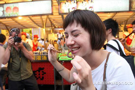 A foreign tourist eats a snack at the Donghuamen food street in Beijing, August 13, 2008. [Asianewsphoto]