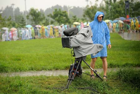 Spectators behind a cameraman leave as the races of canoe/kayak-slalom are postponed to tomorrow, at Shunyi Olympic Rowing-Canoeing Park in Beijing, China, Aug. 14, 2008. The races of canoe/kayak-slalom are postponed to Aug. 15 due to the rain.