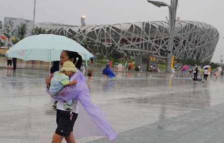A mother holding her baby walks past the National Stadium, also known as the 'Bird's Nest', in rain in the Olympic Green park in Beijing, capital of China, Aug. 14, 2008. A heavy rain hit Beijing Thursday, causing delay of some competitions at the Beijing Olympic Games.