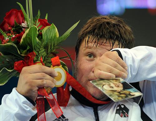 Germany's Matthias Steiner wins the gold in the men's +105kg weightlifting class, showing a picture of his wife on the podium. 