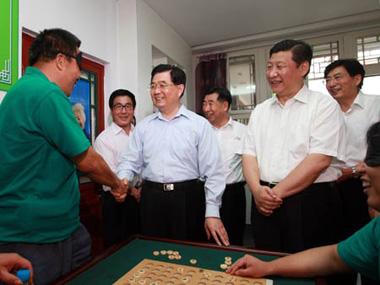 Chinese President Hu Jintao shakes hands with a disabled man who is playing chess in Shichahai community home for the disabled in Beijing. [Xinhua]