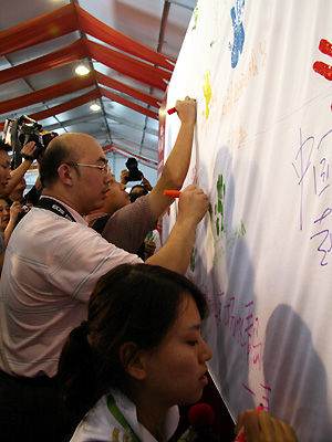 Journalists write messages and leave handprints on a huge scroll created to commemorate the 2008 Beijing Olympics. The scroll writing event was launched at the Beijing International Media Center (BIMC) on August 22. [Wu Huanshu, Wang Yichen/China.org.cn] 