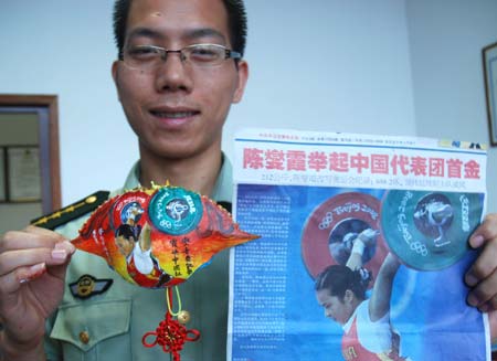 Border police officer Huang Baobang displays his work of a crab shell with the portrait of Chinese weightlifting player Chen Xiexia (L) and the archetype on the newspaper in Zhoushan, east China&apos;s Zhejiang Province, Aug. 24, 2008. Huang draws the pictures of Olympic winning athletes, logos of the Beijing Olympics, and Chinese characteristic patterns on more than 100 crab shells during the Beijing 2008 Olympic Games.