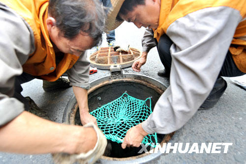 Workers fix a protective web across a sewer manhole on Wednesday, August 27, 2008. [Photo: Xinhuanet]