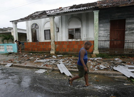 A boy walks through the streets as a woman cleans her home in the aftermath of Hurricane Gustav in Paso Real de San Diego, Cuba August 31, 2008. Gustav moved into the oil-rich Gulf of Mexico on Saturday where it was expected to strengthen and threaten New Orleans after its 150 mile per hour (240 kph) winds cut a swath of destruction through western Cuba. [Agencies] 