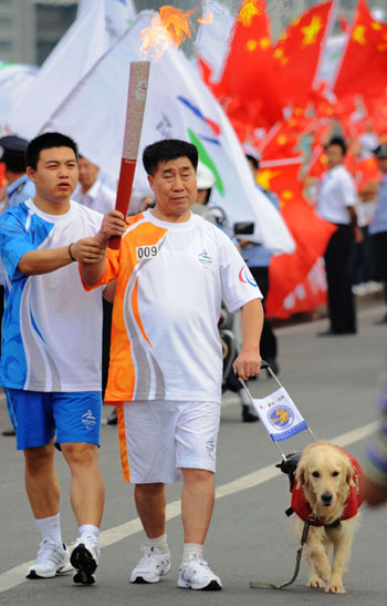 Zhang Dehong (right) holds the Paralympic torch with the help of a torch escort and a guide dog during the Dalian relay on Wednesday. [Xinhua] 