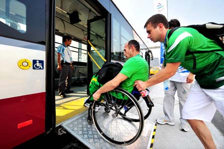 A Paralympic athlete rolls his wheelchair up a ramp with the help of a team staff member to get onto a bus in this picture taken on September 3, 2008. [Xinhua] 