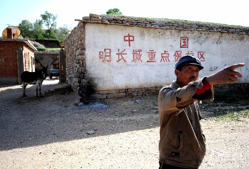 In the picture taken on June 1, 2008 a farmer from the Beibao Village, Qingshuihe County of Inner Mongolia Autonomous Region introduces the situation of the relics of the Great Wall to Xinhua reporter. The Chinese characters on the wall behind are 'the main protection region of China Ming Dynasty Great Wall'.