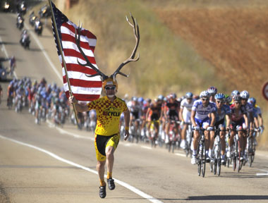 A spectator holding a US flag and wearing antlers runs with the pack of riders during Stage 16 of the Spanish Vuelta between Ponferrada and Zamora on Tuesday.