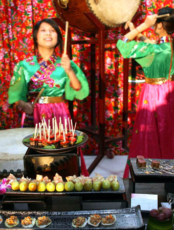 Two girls drum to cheer at a booth of north China cuisine during 2008 Autumn/Winter Food Fair in Shanghai, China on Sep. 17, 2008. Some 150 chefs participated in the fair to show their unique cuisine. (Xinhua/Zhang Ming)