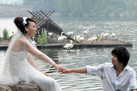 A couple has their photos taken with swans in the backdrop near the West Lake in Hangzhou, East China's Zhejiang Province, September 23, 2008. Twenty white swans were moved from the Hangzhou Zoo to the scenic West Lake, a popular tourist spot, ahead of the National Day holiday. [CFP]