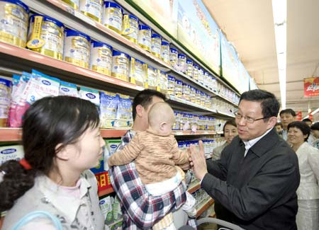 Chinese Minister of Commerce Chen Deming (R) plays with a baby held in the arms of his father who came to buy milk products at a supermarket in Beijing, Sept. 26, 2008. 
