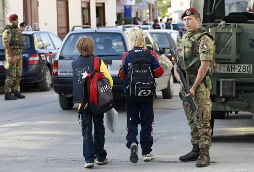 Children walk past Italian paratroopers who patrol a street in Casal di Principe, near Caserta , southern Italy on October 4, 2008. Italian Interior Minister Roberto Maroni said the day before that some 500 paratroopers will deploy to the Naples area at the weekend to join the fight against the local Camorra mafia and will man checkpoints, conduct weapons searches, protect &apos;at-risk&apos; shops and patrol suspects under house arrest. [AFP]