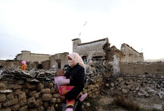 A woman with her child walks past the collapsed building in Gedar Village of Yangbajain Township, Damxung County in southwest China's Tibet Autonomous Region, Oct. 6, 2008. [Xinhua] 