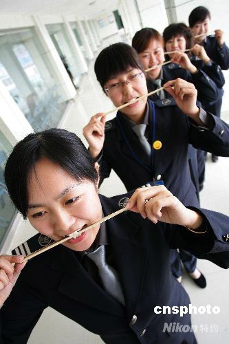 Attendants practice smiles by holding chopsticks in their mouths at the long-distance bus station in Weifang, east China's Shandong Province on Thursday, October 9, 2008. The bus attendants are trained to smile, talk and better behave in the same way ceremonial hostesses for the Olympics were trained. [Photo: cnsphoto] 