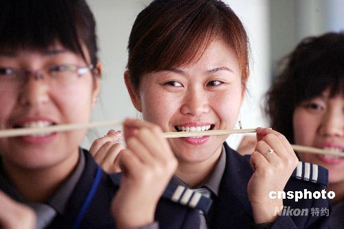 Attendants practice smiles by holding chopsticks in their mouths at the long-distance bus station in Weifang, east China's Shandong Province on Thursday, October 9, 2008. The bus attendants are trained to smile, talk and better behave in the same way ceremonial hostesses for the Olympics were trained.[Photo: cnsphoto] 