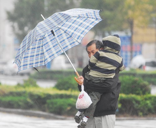 A man protects his child from the rain in Yantai, east Shandong Province on Thursday, October 23, 2008. A strong cold air brought rain and strong wind to the city and its temperature fell to five degrees Celsius. [Photo: Xinhua]