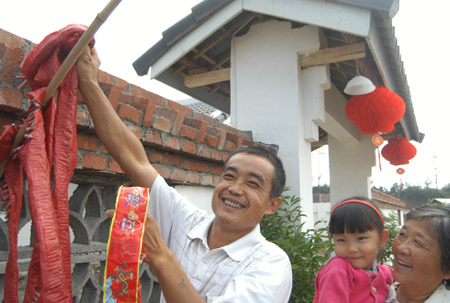 Villager Zhao Guangdong hangs up a string of small firecrackers to celebrate his family's move to a new house in Mianyang, Sichuan, October 23, 2008. Mianyang was badly hit by the May 12 earthquake. [China Daily]