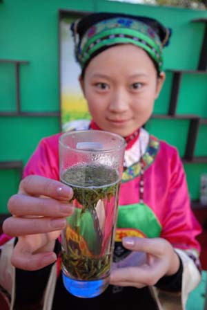 A young lady in costumes of minority groups shows a cup of green tea during a tea promotion activity held in Guiyang, southwest China's Guizhou Province, Oct. 24, 2008. More than 100 tea factories and traders from 38 counties in Guizhou Province exhibited their tea products here Friday.[Xinhua Photo/ Photomall]