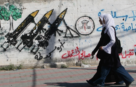 A Palestinian student walks past graffiti showing home-made rockets used by Palestinian militants to fire into Israel in Gaza city Nov. 9, 2008. A senior Hamas leader ruled out chances of implementing a historic Hamas offer for a long-term truce with Israel on Sunday, saying there was no room to implement it in the time being. [Xinhua]