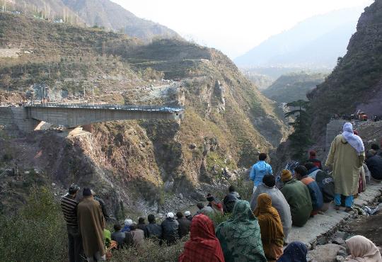 People watch the rescue operations around a collapsed bridge. The bridge under construction over an Himalayan river in Indian-controlled Kashmir collapsed Sunday, killing at least four workers and leaving 19 others missing and feared dead, local police said. 