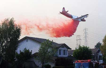 An airplane drops flame retardant on a home as fire burns in Diamond Bar, California November 16, 2008. 