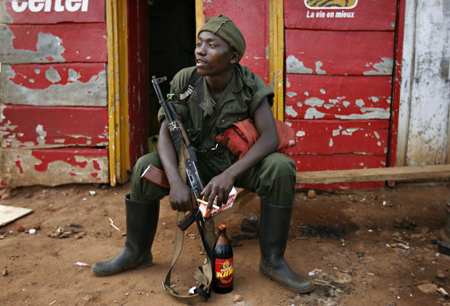 A government soldier sits with a beer outside a looted kiosk after a day of fighting in the village of Kayna in eastern Congo, Nov.18, 2008. 