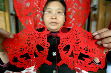 Pan Qiuai, 56, shows her paper-cutting work in her residence in Yanhu District of Yuncheng City, north China's Shanxi Province, November 20, 2008. The work, the result of her one month's effort, comprising 100 bulls in different postures, is a token of her good wish for the coming year, the Year of Ox in Chinese lunar calendar. [Photo: Xinhua] 