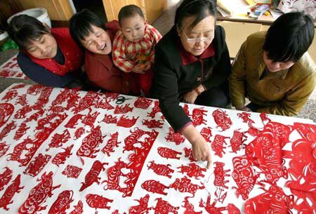 Pan Qiuai (2nd R) explains as her neighbors look at her paper-cutting work. [Photo: Xinhua]