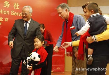 Li Xueju(left), Minister of Civil Affairs, gives asouvenir to a China-born girl who is adopted by an American family. 