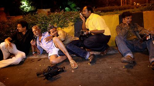 Indian men along with journalists take shield at one of the attack site in Mumbai on November 26, 2008. Nearly 80 people were killed in a series of shootings and blasts across India's financial capital Mumbai late 26 November, the state government said. 