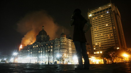 A reporter talks on her phone as smoke is seen coming from Taj Hotel in Mumbai November 27, 2008. Large plumes of smoke were seen rising from the top of the landmark Taj Hotel in Mumbai on Thursday and heavy firing could be heard, a Reuters witness said. 