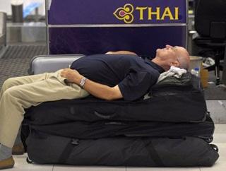 A foreign tourist rests on his luggage while waiting at a check-in counter at Suvarnabhumi International Airport in Bangkok early on November 26. [Pornchai Kittiwongsakul/AFP] 