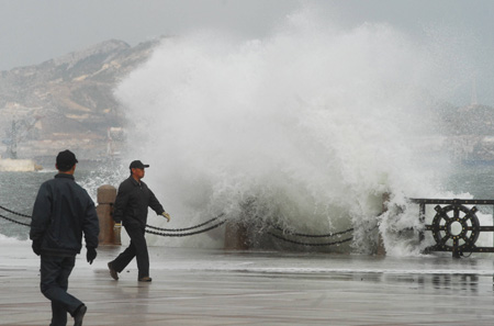 A wave crashes against a sea wall in Yantai, Shangdong province, as people walk by on Thursday. High seas and heavy winds have forced all passenger ships from Yantai to Dalian, Liaoning province, to remain in harbor. 