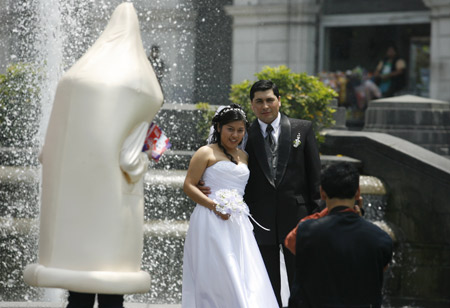 A man dressed as a condom for an AIDS and HIV prevention campaign looks at a recently married couple posing for a wedding photographer in downtown Lima Nov. 28, 2008. [Xinhua/Reuters]