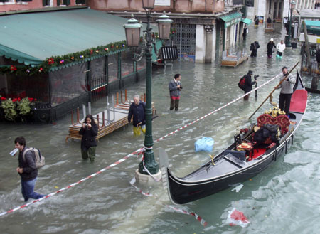 Pedestrians wade through flood waters, past a gondola, in Venice December 1, 2008. Large parts of Venice were flooded on Monday as heavy rains and strong winds lashed the lagoon city, with sea levels at their highest level in 22 years.[China Daily via Agencies] 