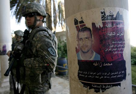 U.S. soldiers stand guard next to a defaced poster of a wanted member of Shi'ite Mehdi Army militia outside a mosque in Hurriya district northwest of Baghdad December 3, 2008.[Xinhua/Reuters]