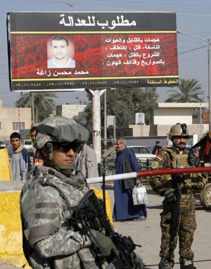 A U.S. soldier (L) of 2nd Heavy Brigade Combat Team, 1st Infantry Division stands guard with an Iraqi soldier below a billboard of a wanted member of Shi'ite Mehdi Army militia outside a mosque in Hurriya district northwest of Baghdad December 3, 2008.[Xinhua]