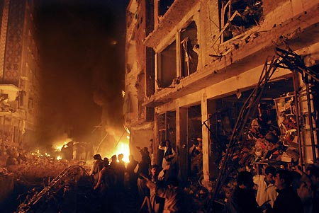 Pakistani people are seen next to a building on fire at the site of an explosion in Peshawar, Pakistan, Friday, Dec. 5, 2008. [Xinhua/AFP]