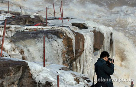 A photographer takes pictures of natural ice creations in front of the Hukou waterfall of the Yellow River, North China's Shanxi Province, December 7, 2008. Hukou waterfall is frozen due to temperature dropping, turning its splashing water beads into ice of various shapes and shades - a great attraction to winter tourists. 