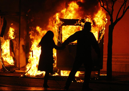 A couple runs to escape a fire from a bus station booth during riots in Athens Dec. 7, 2008. Riots raged in several cities after police shot dead a teenage boy in the Greek capital, in the Mediterranean nation's worst civil disturbances in years. [Xinhua/Reuters]