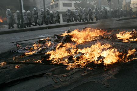 Riot policemen walk next to burning barricades during riots in Athens December 7, 2008. Hundreds of demonstrators clashed with riot police in Athens and the northern Greek city of Thessaloniki on Sunday in a second day of protests at the shooting by police of a 15-year-old boy. [Agencies via China Daily] 