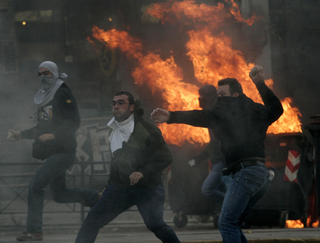  Protesters throw stones at riot policemen behind burning barricades during riots in Athens December 7, 2008. Hundreds of demonstrators clashed with riot police in Athens and the northern Greek city of Thessaloniki on Sunday in a second day of protests at the shooting by police of a 15-year-old boy. [Agencies via China Daily] 